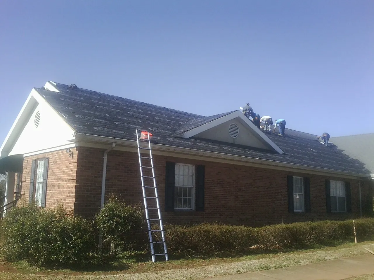 Crew tearing shingles off a brick ranch roof with a ladder set — Emergency Roof Repair work by our crew in Minster