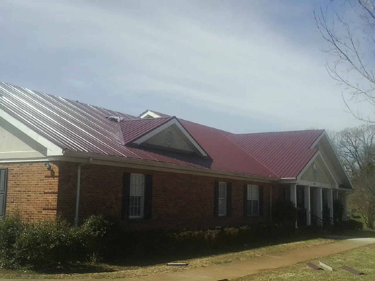 Red metal roof with gabled entries on a long brick building, from a Hail Damage Roof Repair job in Minster