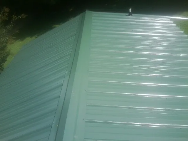 New green metal panels meeting at the ridge of a roof — Flat Roof Repair work by our crew in Minster