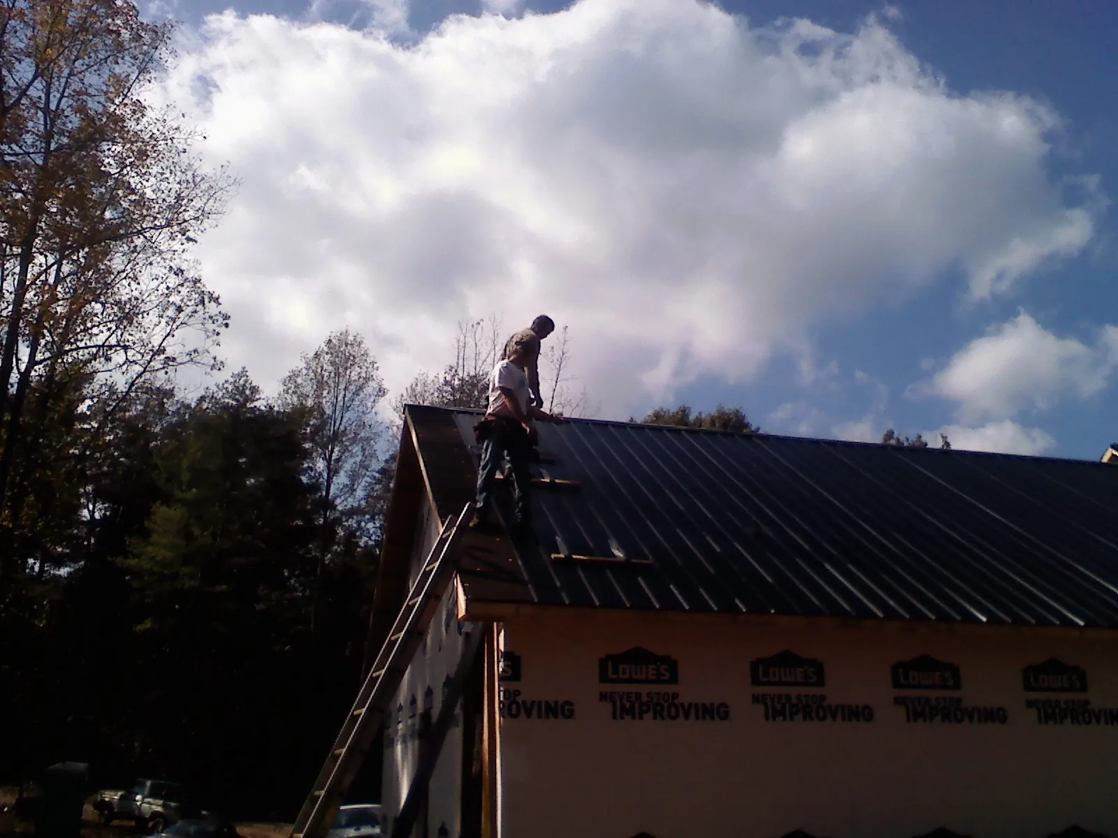 Roofer fastening dark metal panels high against a cloudy sky, from a Roof Inspection job in Minster