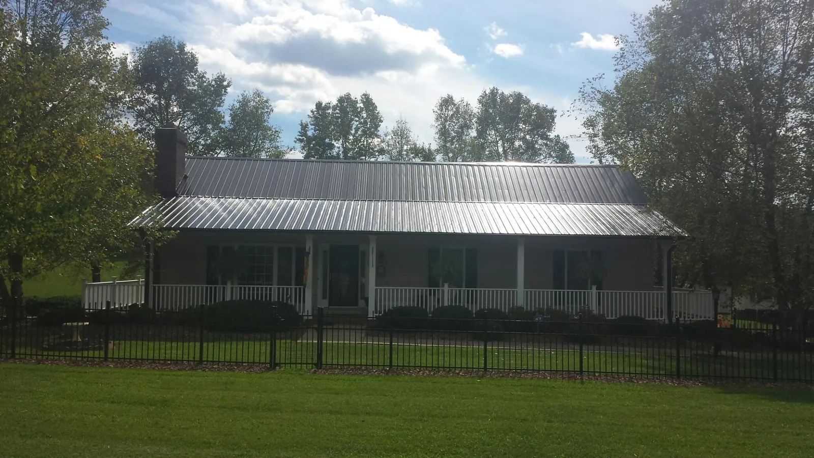 Gray metal roof on a brick ranch with a full width front porch — Gutter Guard Installation work by our crew in Minster
