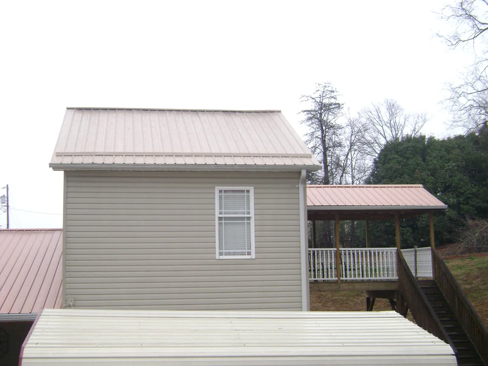 Tan metal roofs on a two story addition and attached porch, from a Roof Replacement job in Minster